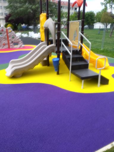Tobogán y escaleras en un parque infantil con suelo de goma amarilla y morada.